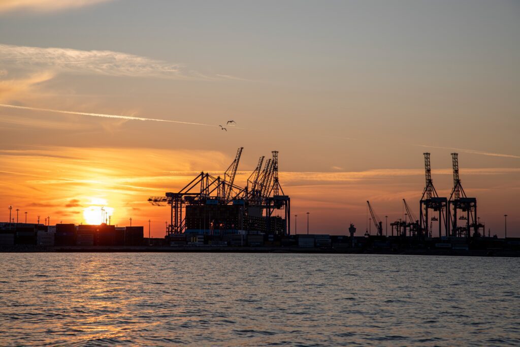 Silhouette of port cranes at sunset over water, symbolizing international trade.