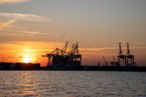 Silhouette of port cranes at sunset over water, symbolizing international trade.