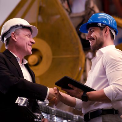 Two professionals in hard hats concluding a deal with a handshake in a factory.