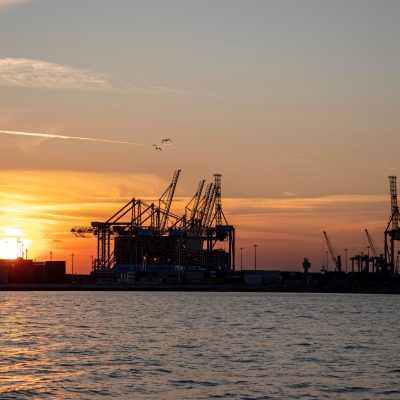 Silhouette of port cranes at sunset over water, symbolizing international trade.